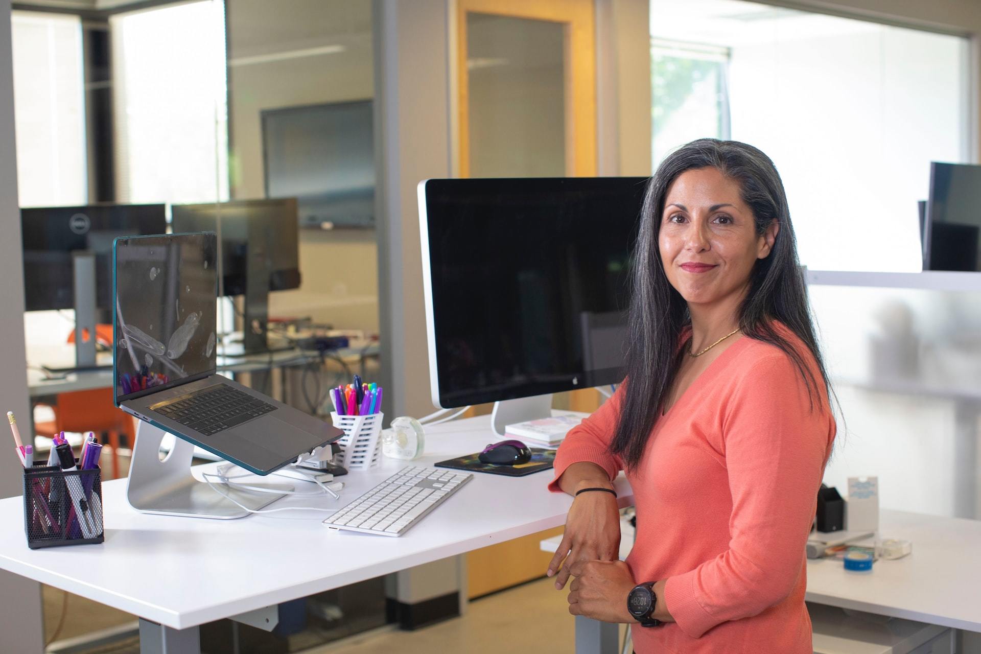 A woman standing proudly next to a stand-up desk with a computer.